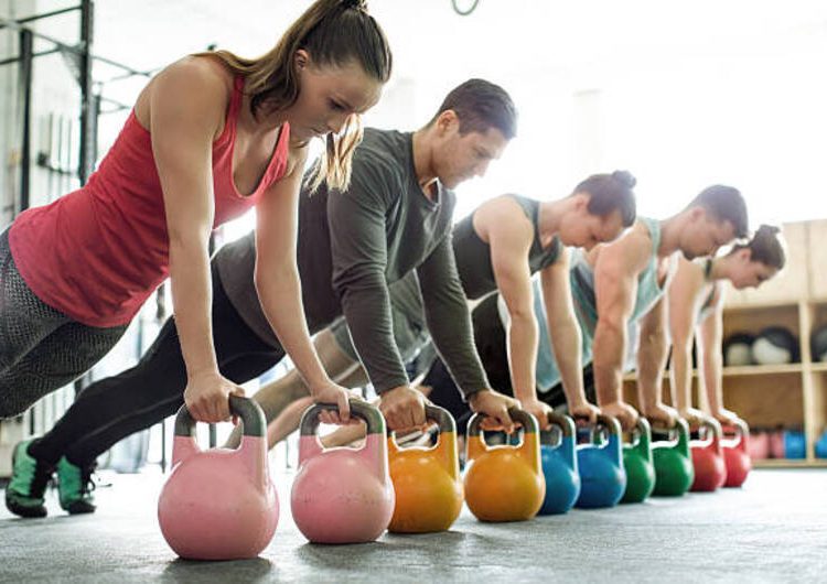 Group of young men and women doing push-ups on kettlebells in a gym